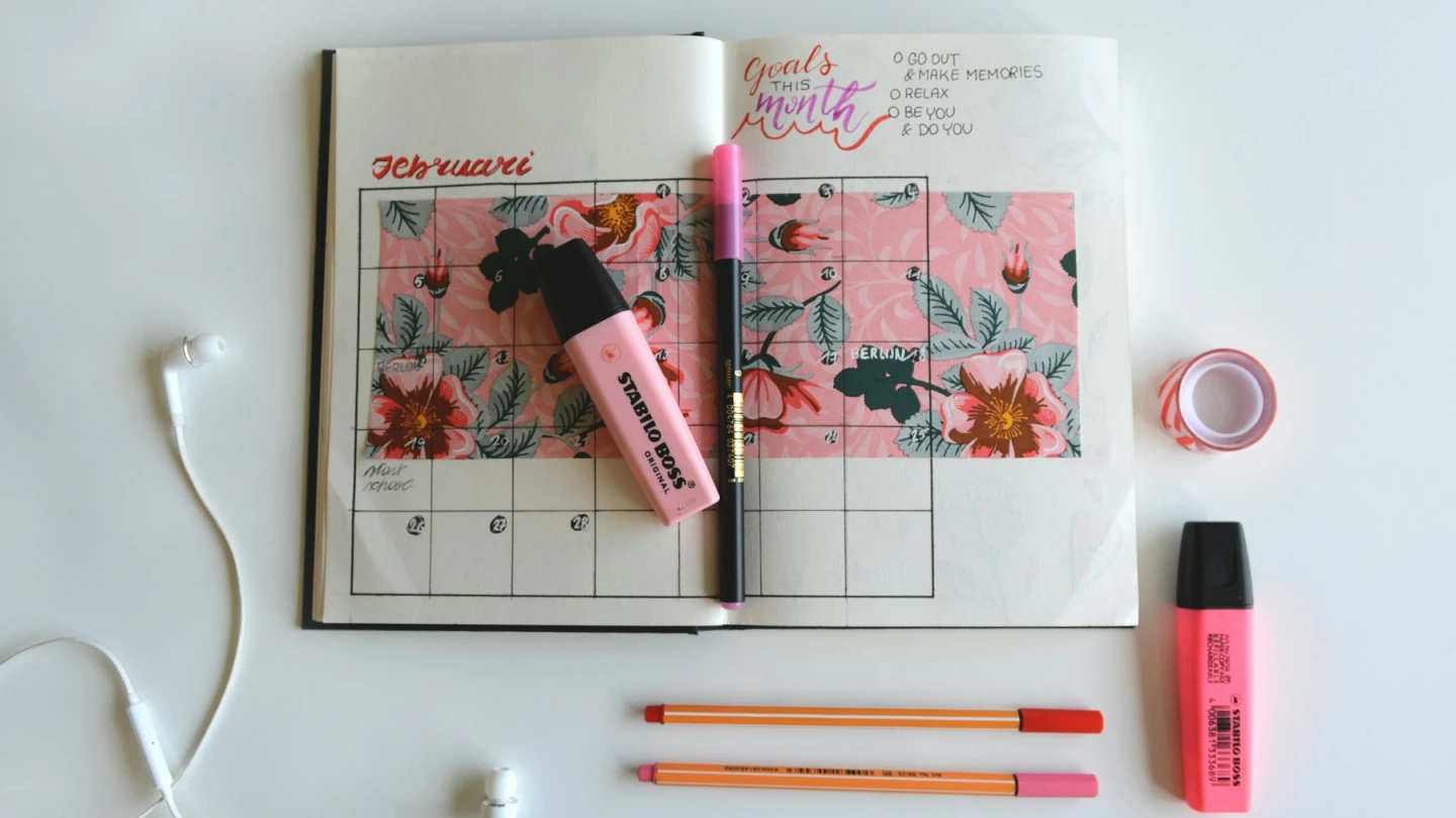 An open monthly calendar with pens and highlighters arranged on a light desk.