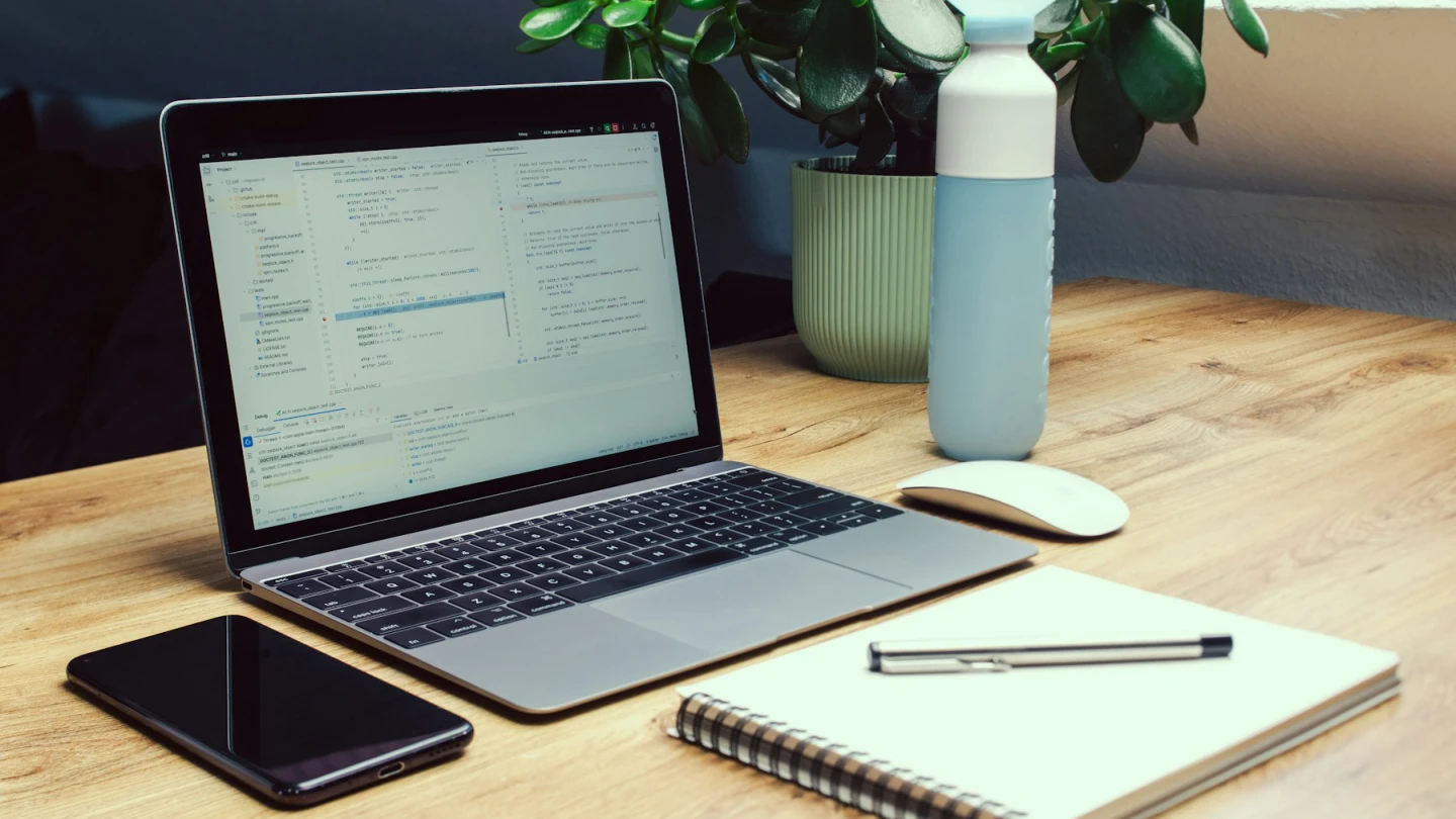 A laptop, phone, notebook, and pen arranged together on a home desk.