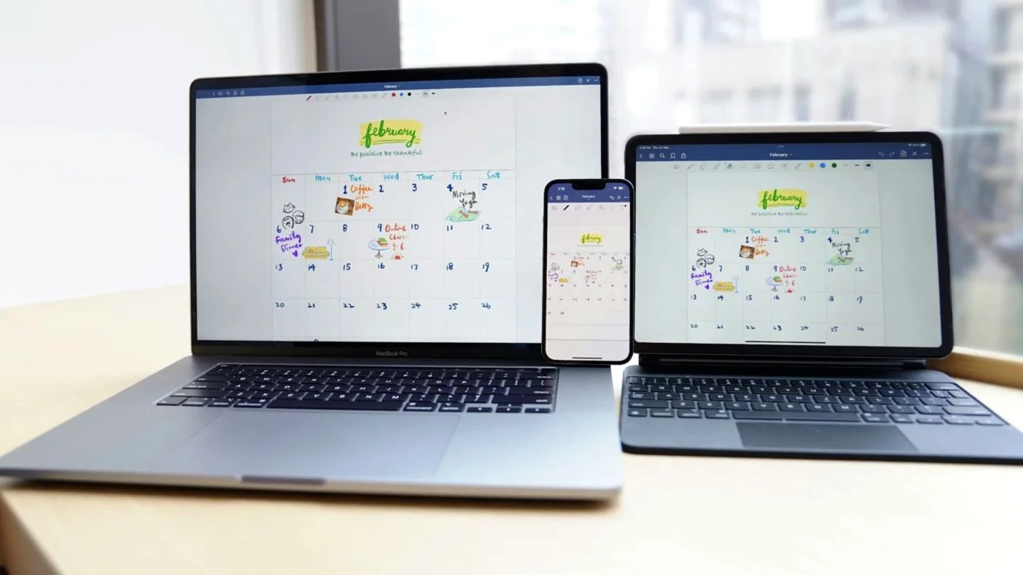 A digital family calendar synchronized across a laptop, phone, and tablet on a bright home desk.